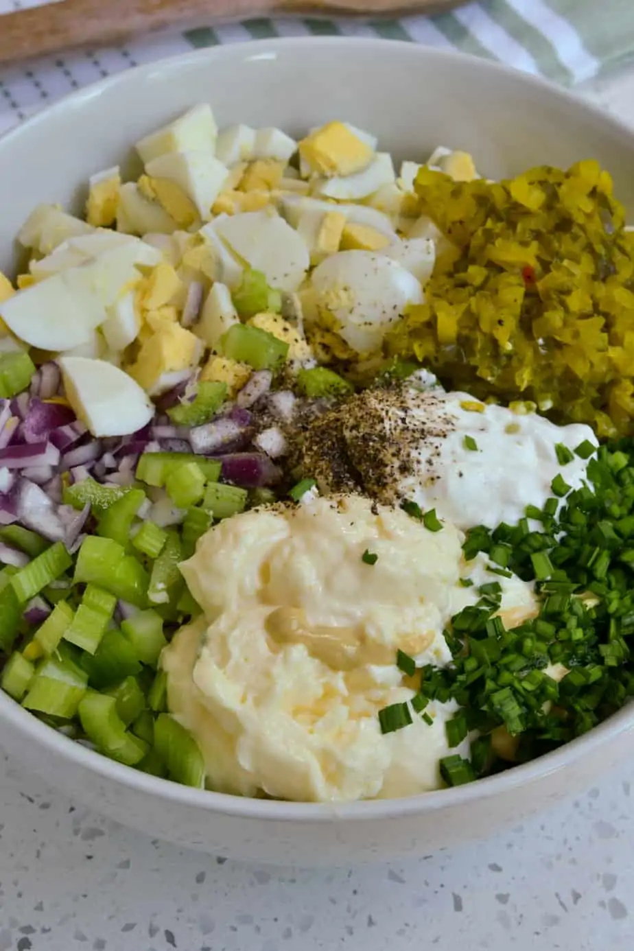 Potatoes, mayonnaise, mustard, celery, red onion, hard boiled eggs, pickle relish and chives in a bowl. 