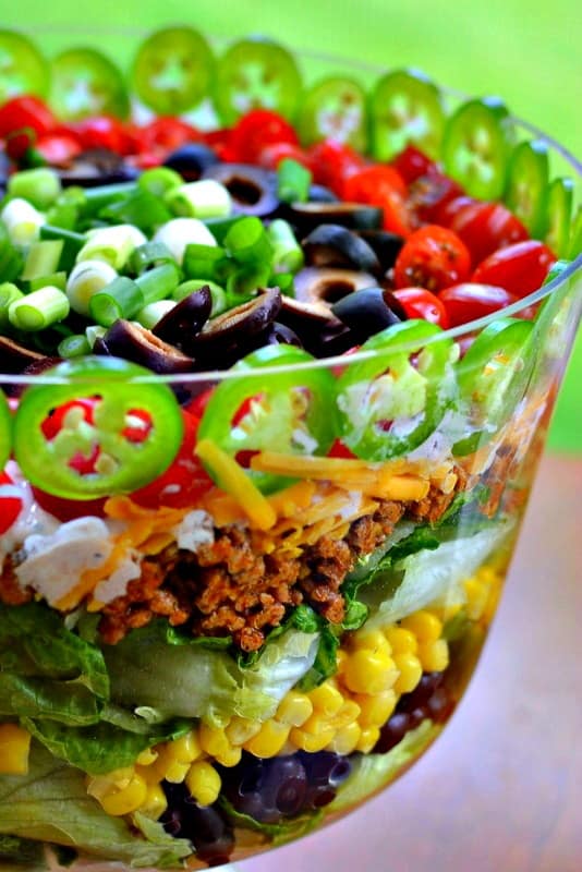 Layered Taco Salad is a gorgeous layered salad of romaine, black beans, corn, seasoned beef, cheddar cheese, tomatoes, black olives, green onions, and jalapenos with a simple sour cream and salsa dressing.