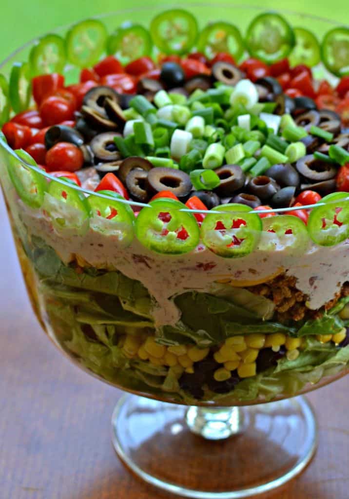 A beautiful layered taco salad recipe made with seasoned ground beef or turkey, romaine and iceberg lettuce, shredded cheddar, sweet tomatoes, black olives, crisp green onions and spicy jalapenos.  