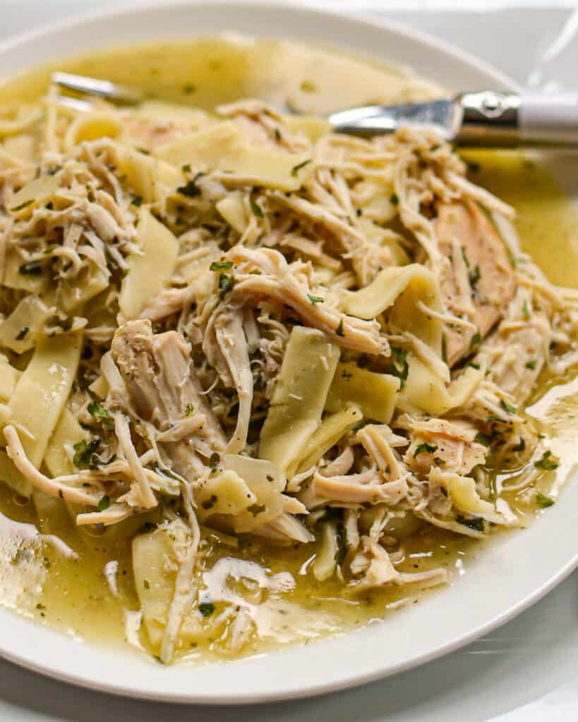 Tender Crockpot Chicken and Noodles Crockpot Chicken and Noodles on a white plate with a fork.