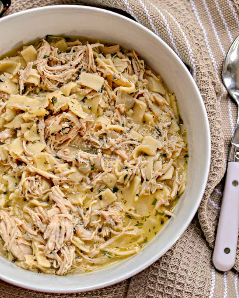 Weeknight Crockpot Chicken and Noodles Crockpot Chicken and Noodles in a white bowl with a spoon off to the right.