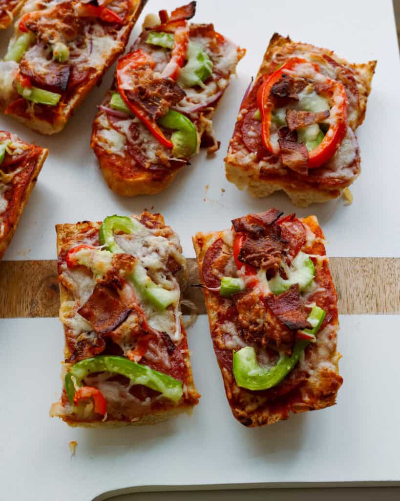 A close up view of French bread pizza on a white wooden serving board. 
