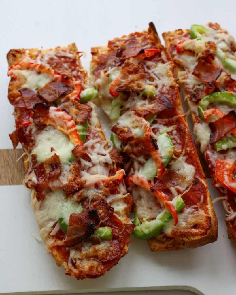 Two long slices of French bread pizza with pepperoni, bacon, and bell peppers. 