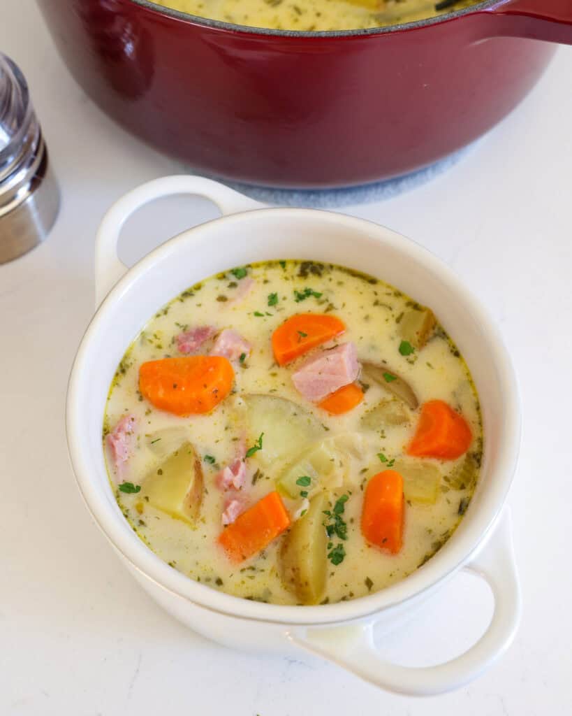 Creamy Ham and Potato Soup A single serving bowl full of ham and potato soup with a salt and pepper shaker in the background.