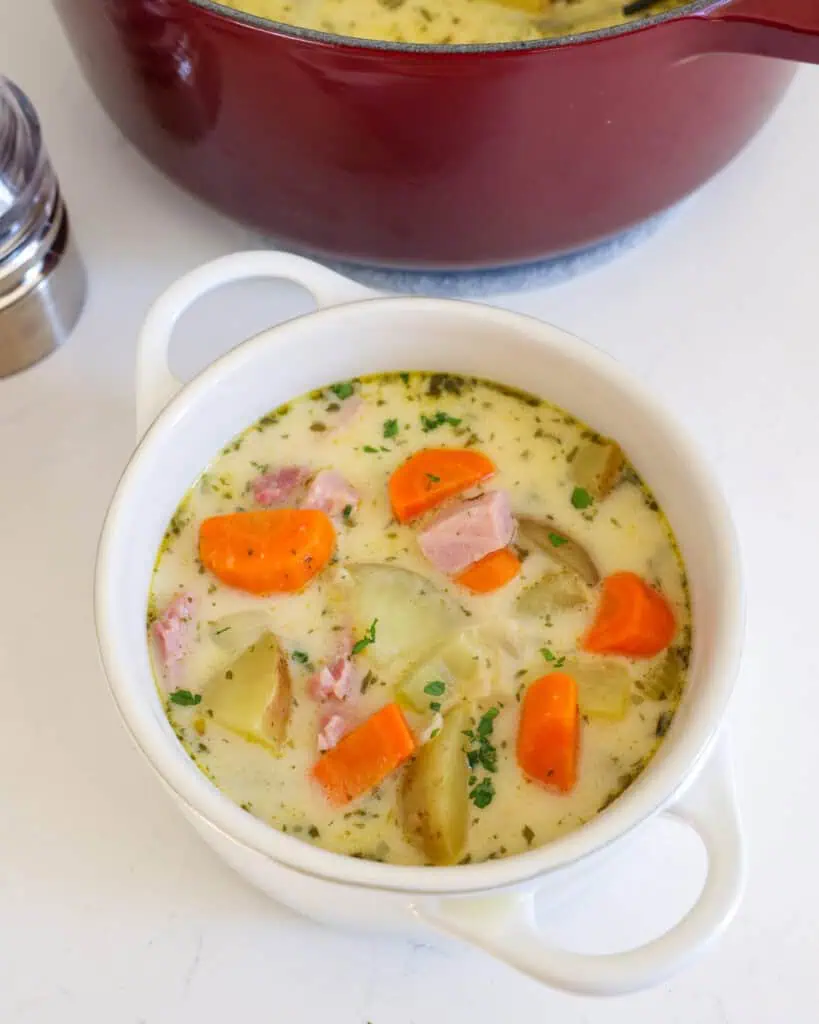 Creamy Ham and Potato Soup A single serving bowl full of ham and potato soup with a salt and pepper shaker in the background.