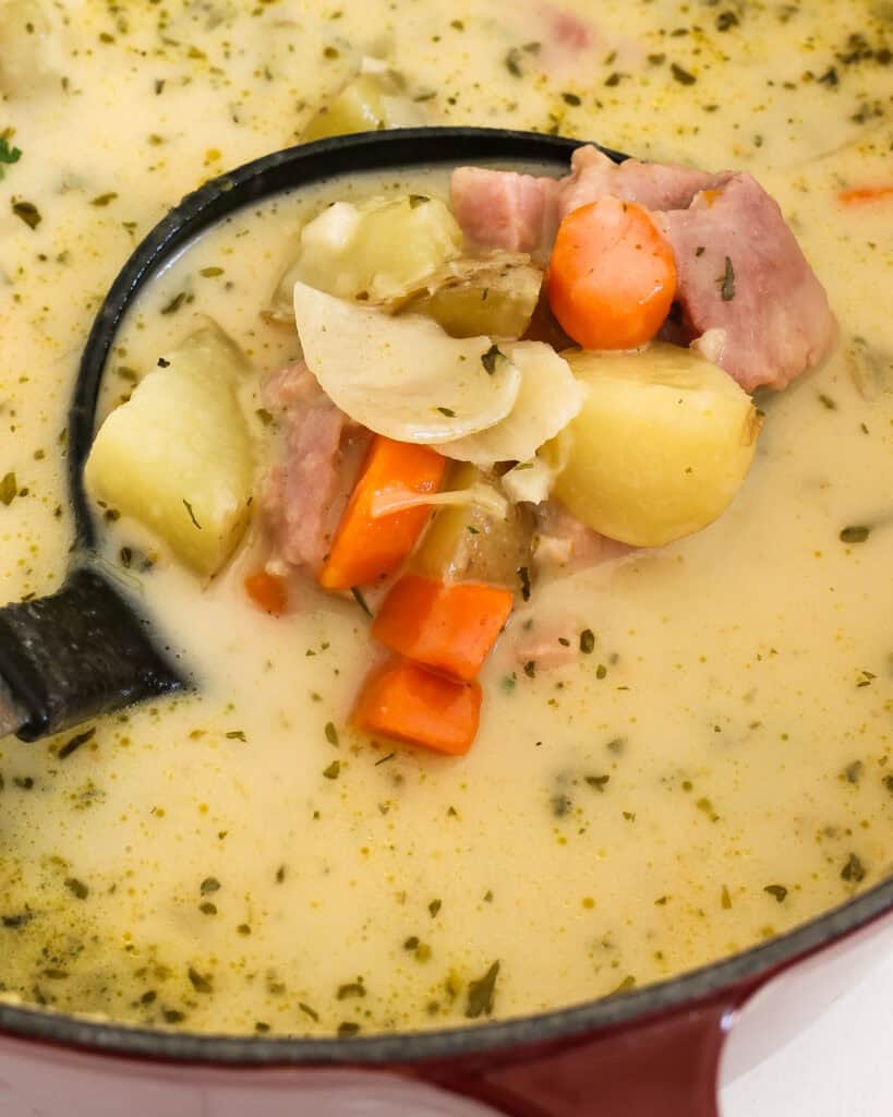 A close up view of a ladle full creamy ham and potato soup.