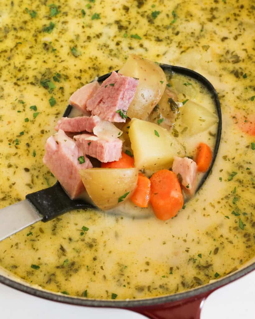 A Dutch oven and ladle full of creamy ham and potato soup.