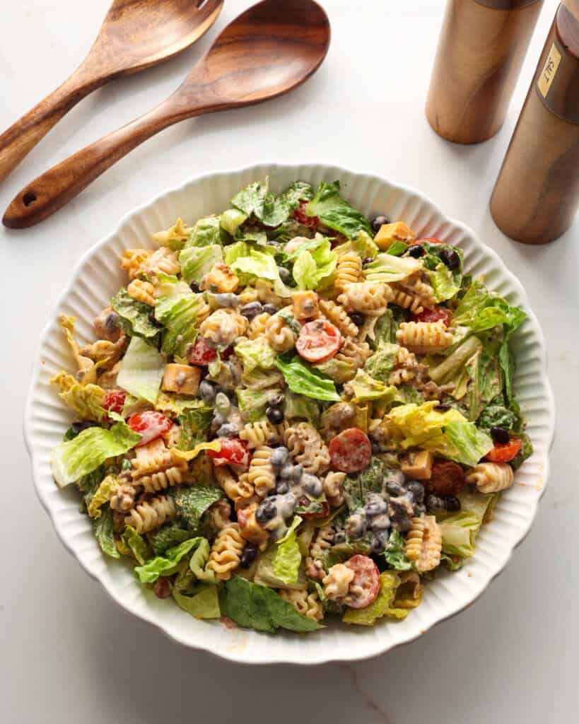 An overhead view of tacos pasta salad with wooden utensils and salt and pepper shaker in the background. 