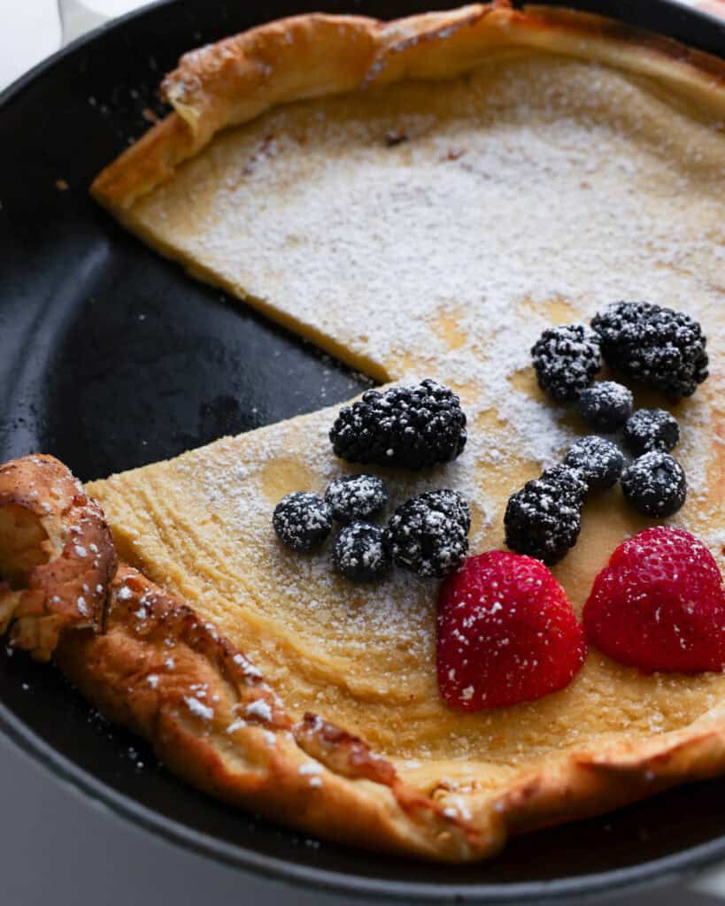 A close up view of a Dutch baby pancake with powdered sugar and fresh berries. 
