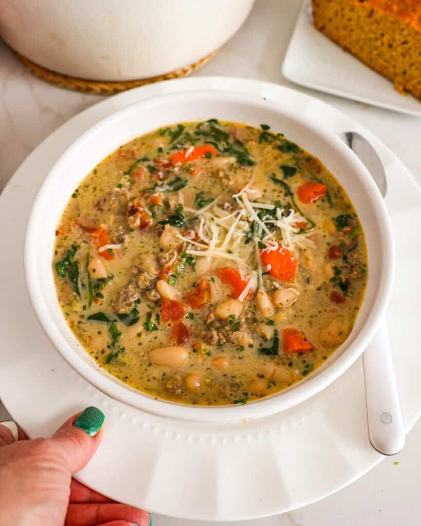 Bowl full of Tuscan white bean soup garnished with parsley and Parmesan cheese. 