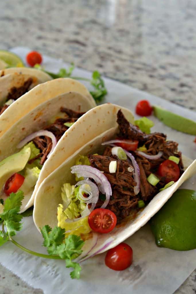 Serve your Beef Barbacoa Tacos in flour tortillas topped with onions, tomatoes, and lettuce