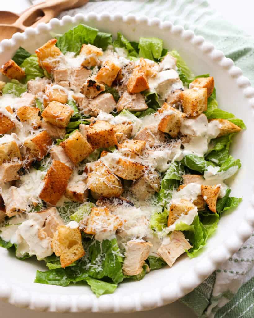 A close up view of romain lettuce with grilled chicken, croutons, Caesar dressing, and Parmesan cheese. 