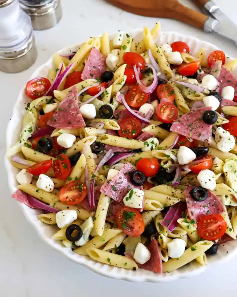 A close up view of Italian pasta salad with penne pasta, salami, black olives, mozzarella cheese, artichoke hearts, grape tomatoes, sweet red onions, and freshly grated Parmesan cheese tossed lightly with homemade Italian dressing.