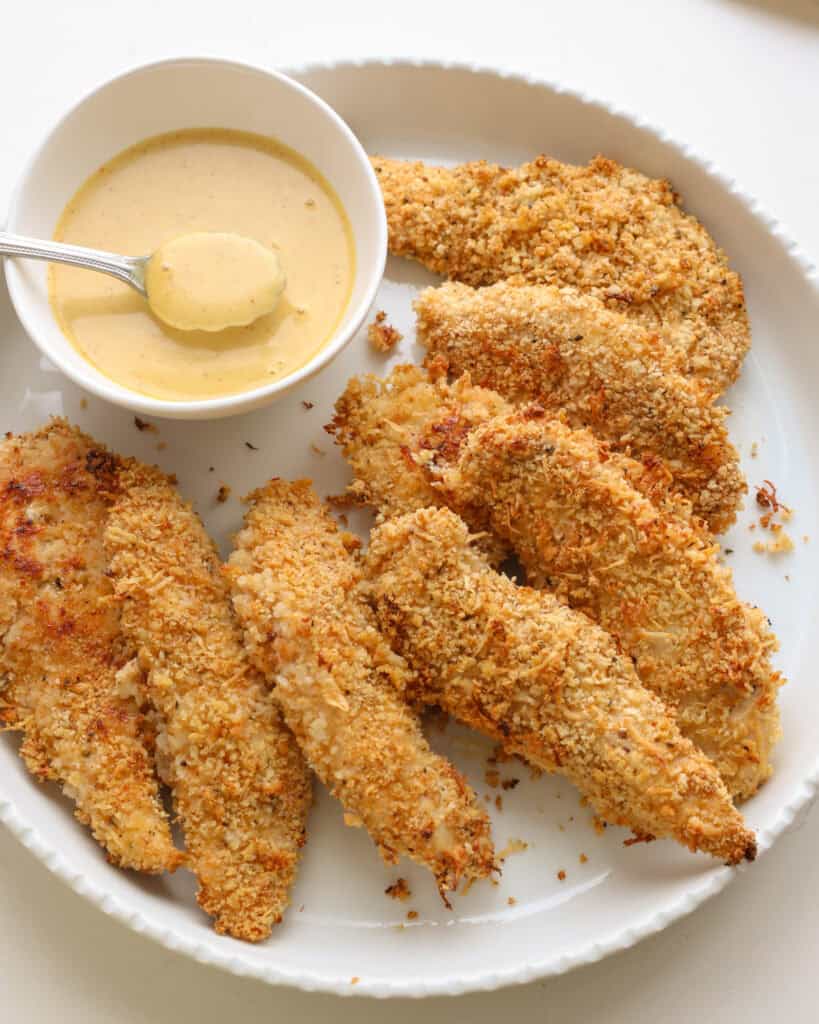 Honey Mustard Sauce A round circle platter full of chicken tenders with honey mustard sauce.
