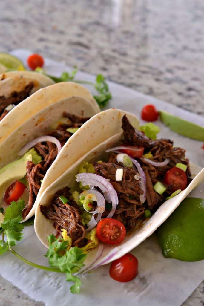 Top your slow cooker Barbacoa Tacos with your favorite toppings like onions, tomatoes and lettuce