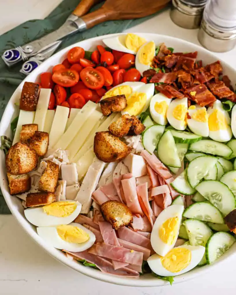 Chef Salad Recipe An overhead view of a chef salad with boiled eggs, cheese, tomatoes, cucumbers, ham, turkey, and bacon.