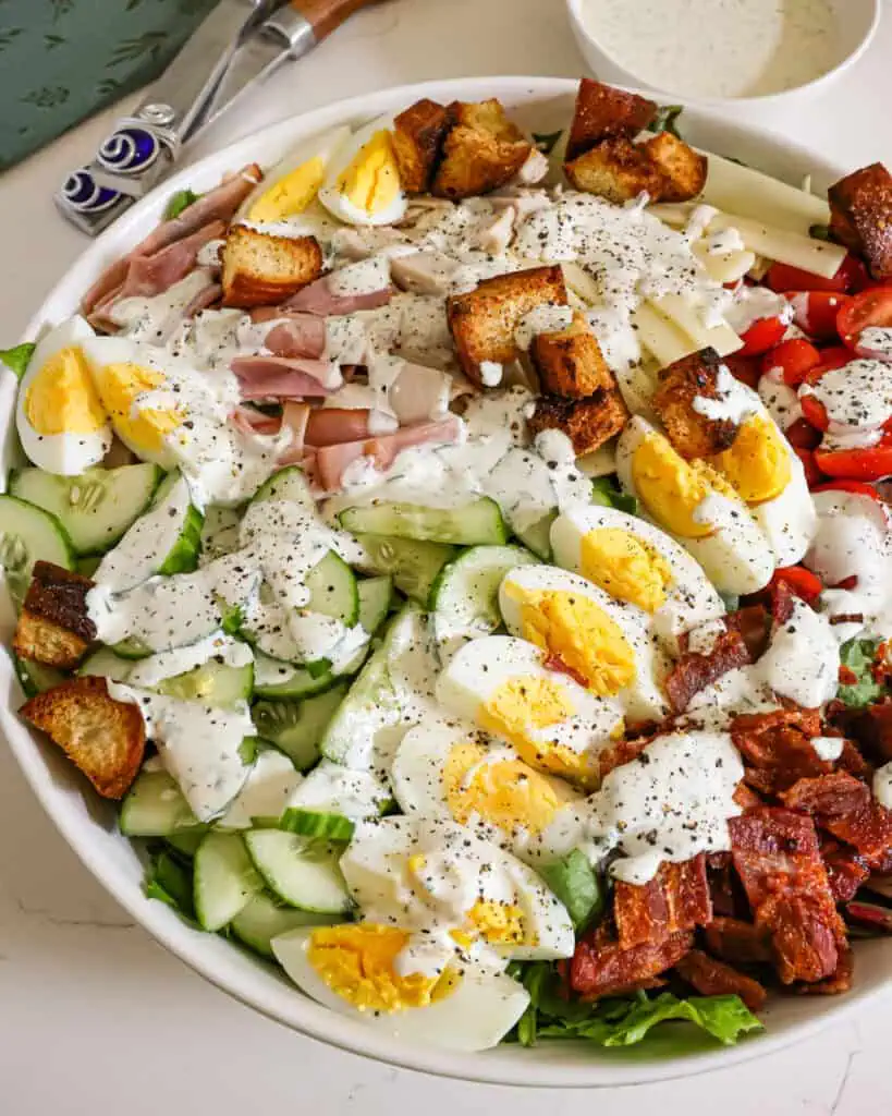 Chef Salad A close up view of a large bowl of chef salad with ranch dressing drizzle over it.