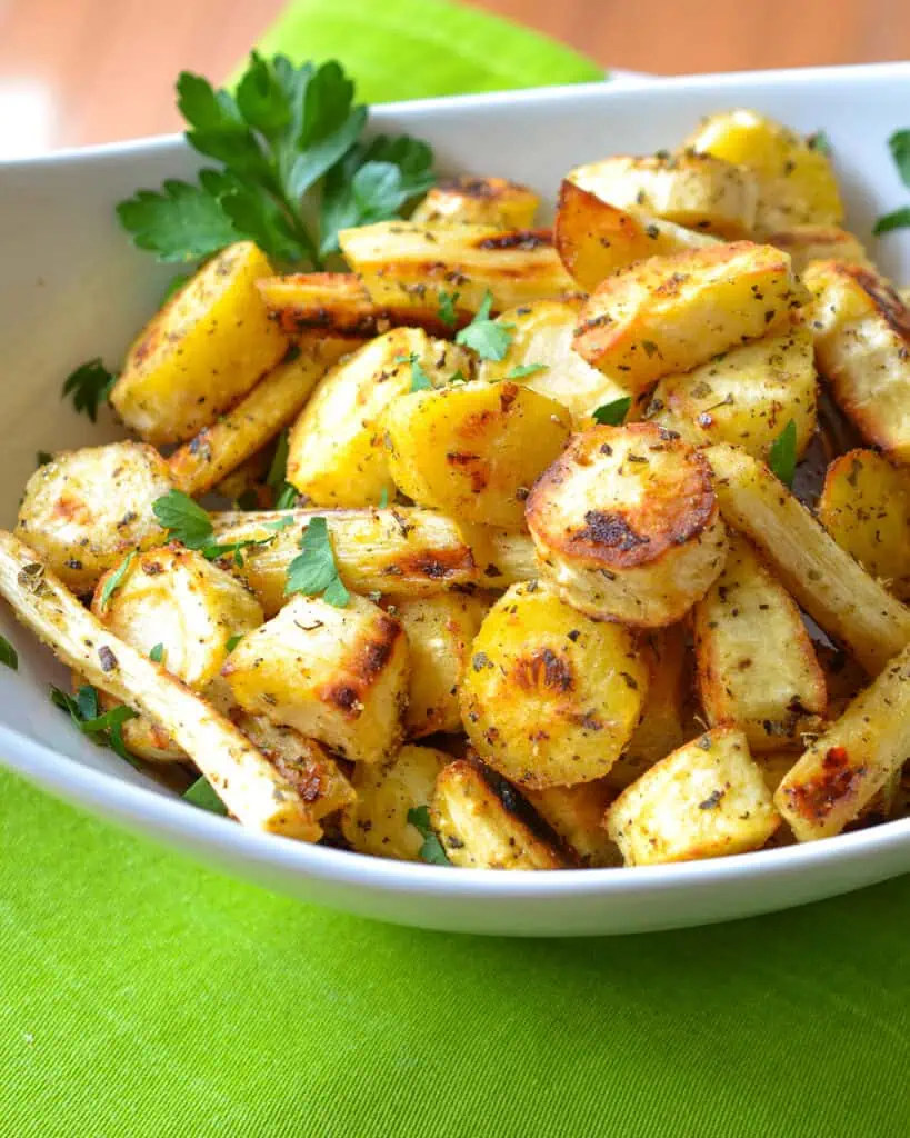 A close up view of roasted parsnips garnished with parsley in a while serving bowl. 