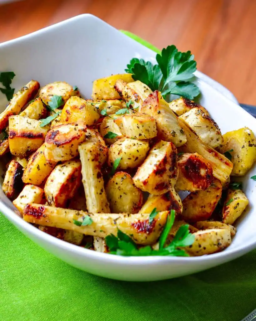 Roasted parsnips in a serving bowl over a green kitchen towel. 