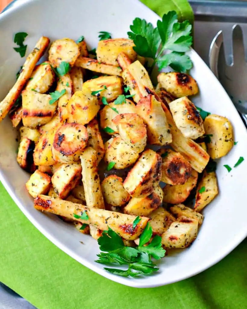 Tender roasted parsnips perfectly seasoned and roasted to a crisp golden brown in a white serving bowl. 