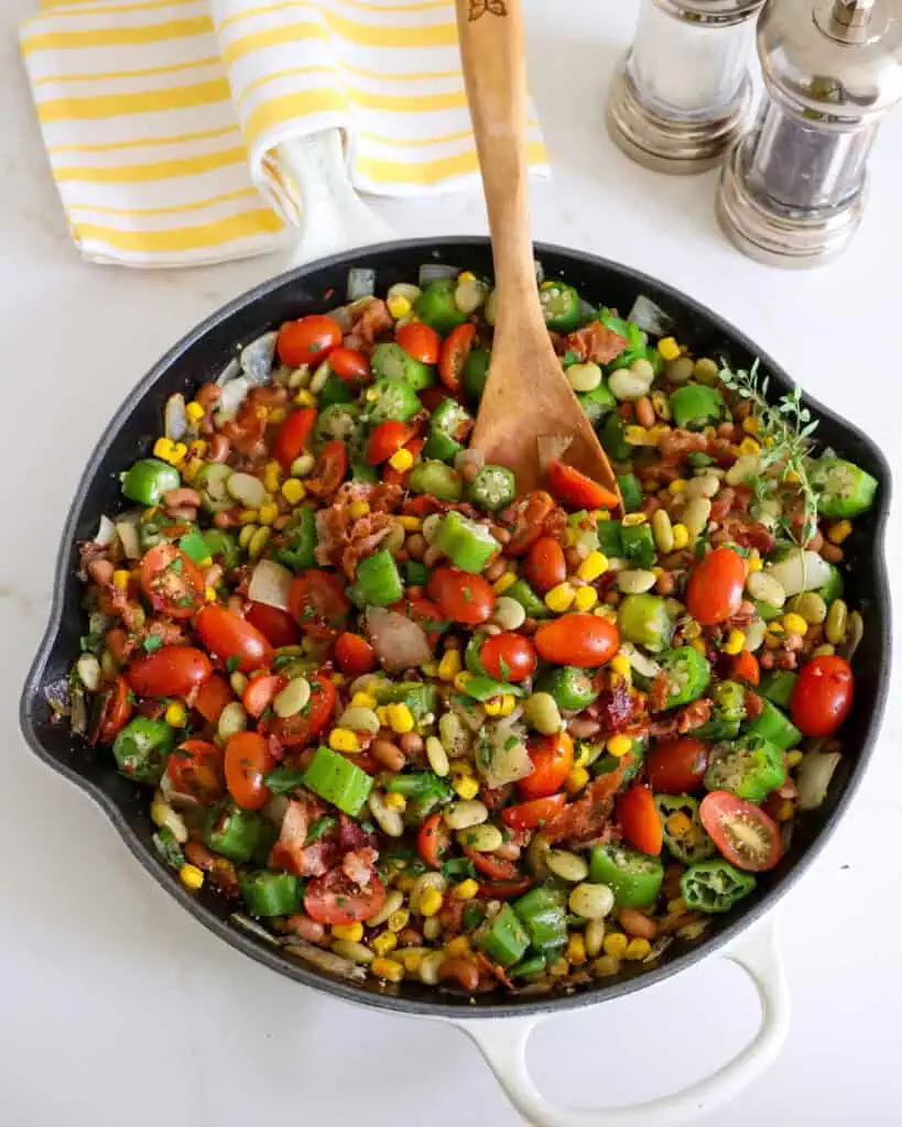 An overhead view of summer succotash with lima beans, black-eyed peas, sun-ripened tomatoes, sweet corn, onions, garlic, okra, and crisp smoked bacon