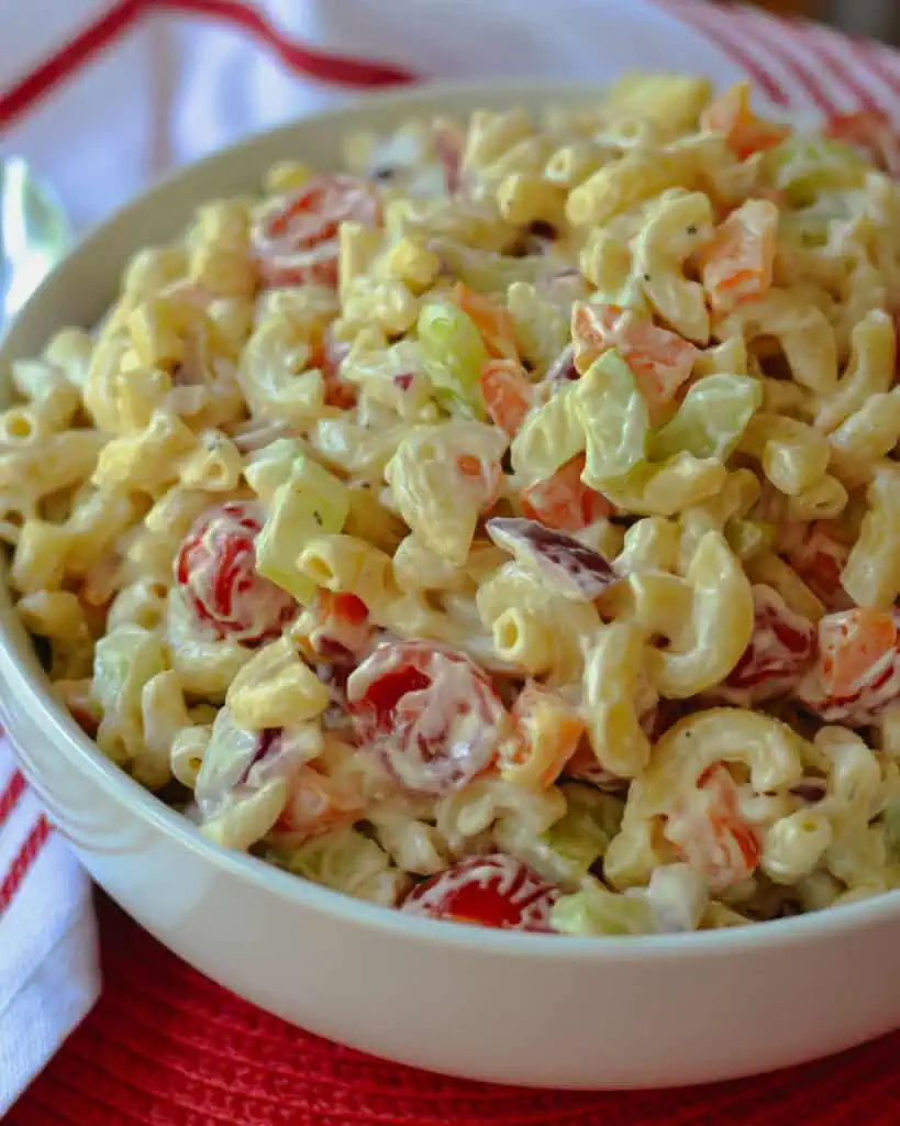 Macaroni salad in a large white sserving bowl with a red and white kitchen towel in the background.