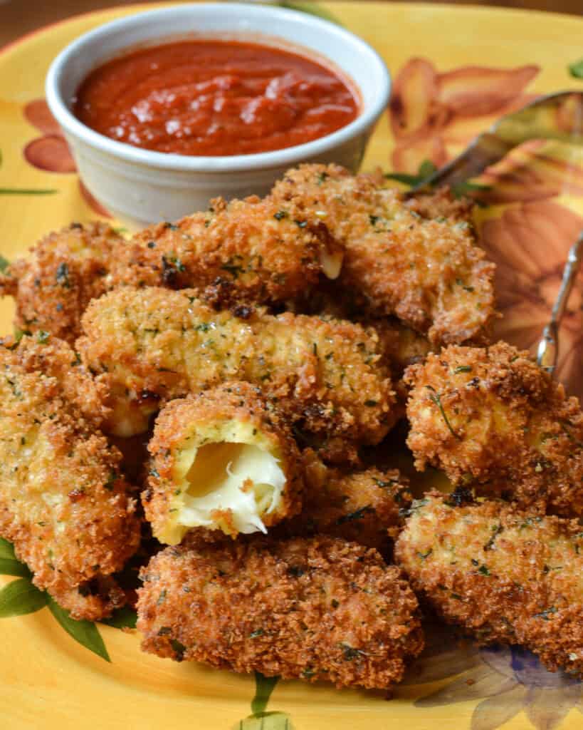 A plate full of mozzarella sticks with a bowl of marinara.