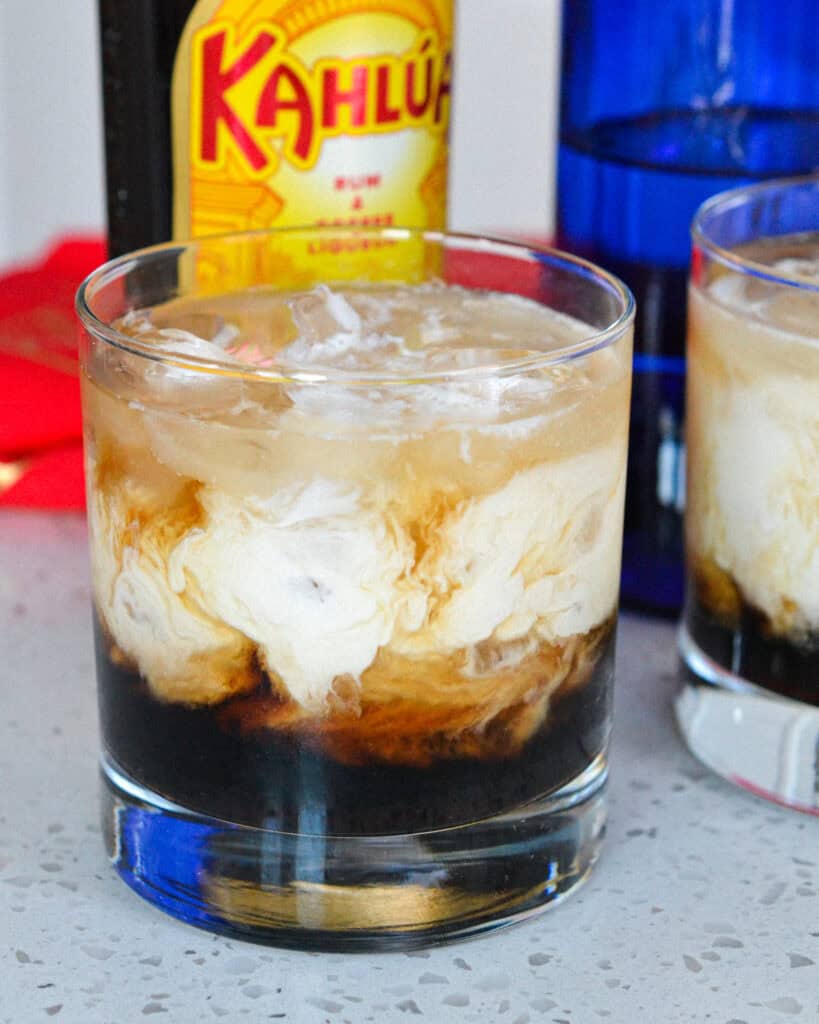 A white Russian cocktail in front of a bottle of Kahlua