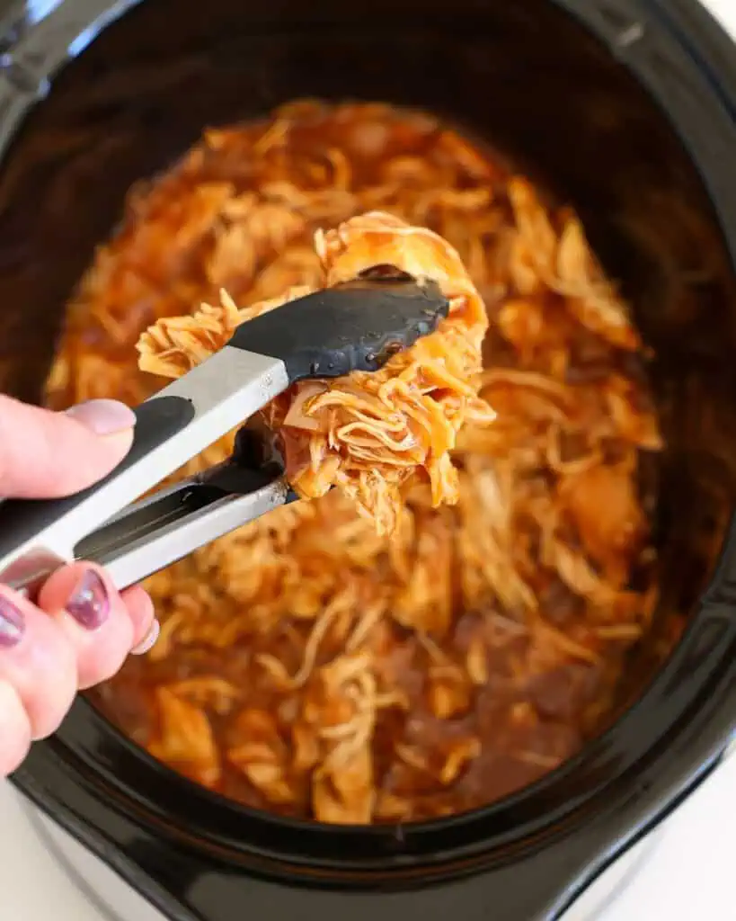 Slow Cooker BBQ Pulled Chicken Tongs full crock pot pulled chicken over a slow cooked full of cooked pulled chicken.