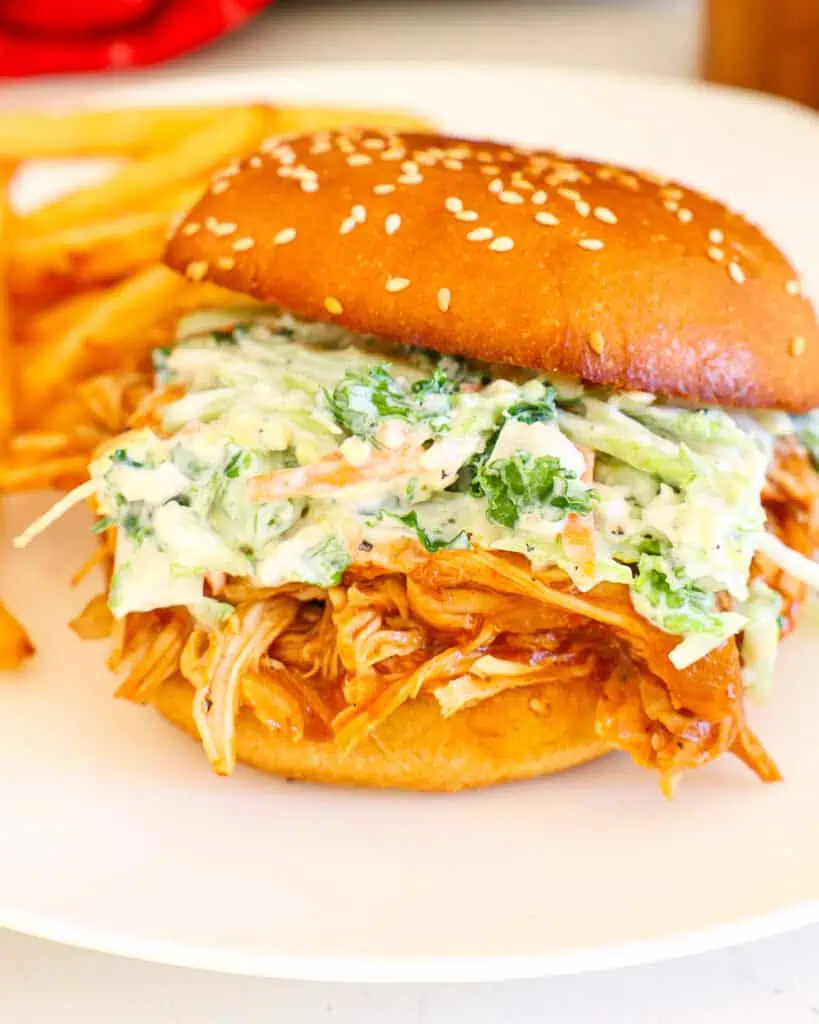 Slow Cooker Pulled Chicken Slow cooker pulled chicken on brioche bun with coleslaw amd French fries in the background.