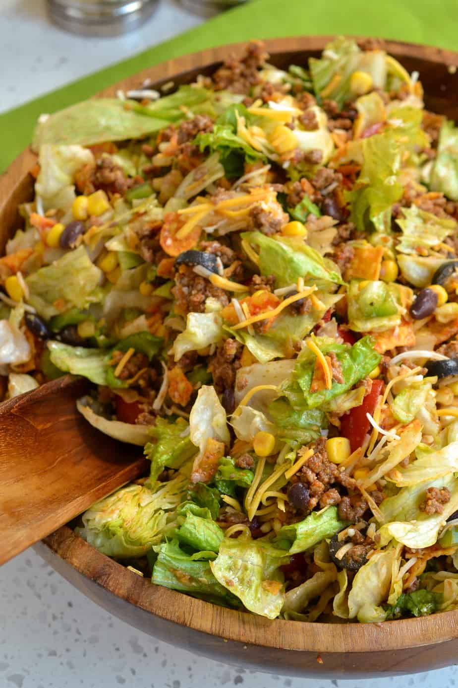 Doritos Taco Salad is a delectable combination of iceberg lettuce, tomatoes, green peppers, black beans, corn, black olives, seasoned ground beef, shredded cheddar jack cheese, and crunchy Doritos in a homemade tangy sweet Catalina dressing