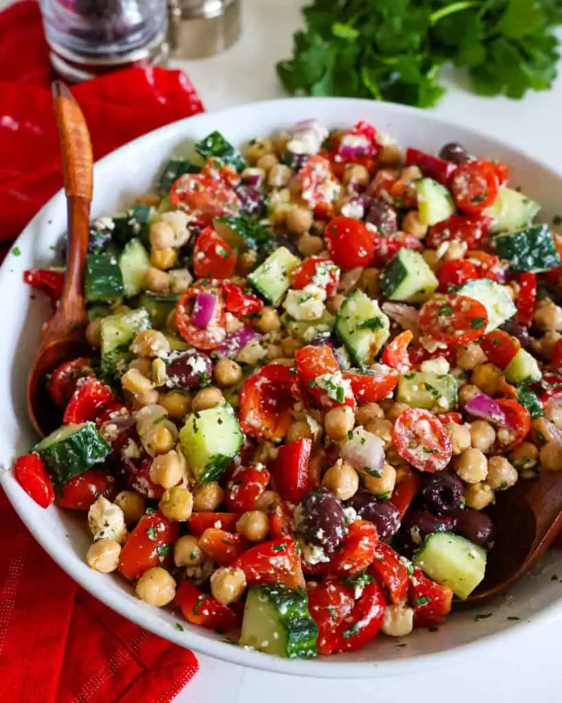 A bowl full of chickpea salad with two wooden spoons in it. 