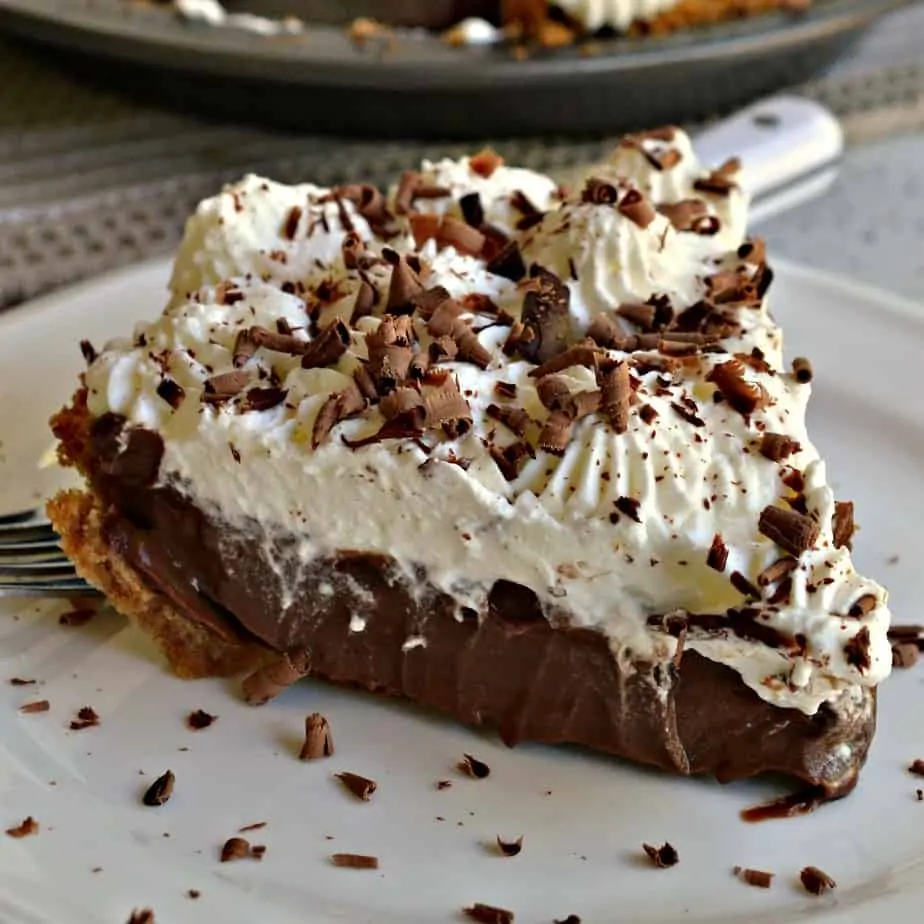 A decadently rich chocolate pie nestled in a graham cracker crust garnished with fresh whipped cream and chocolate shavings.