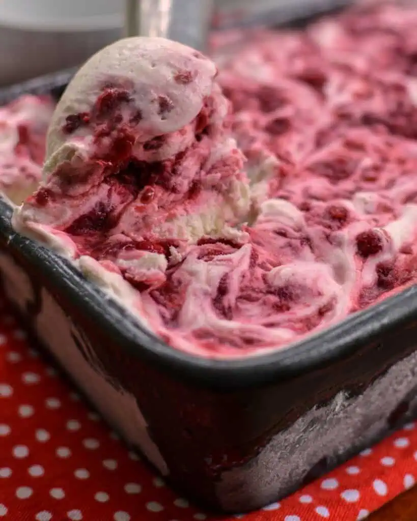 A loaf pan and an ice cream scooper full of raspberry ice cream. 