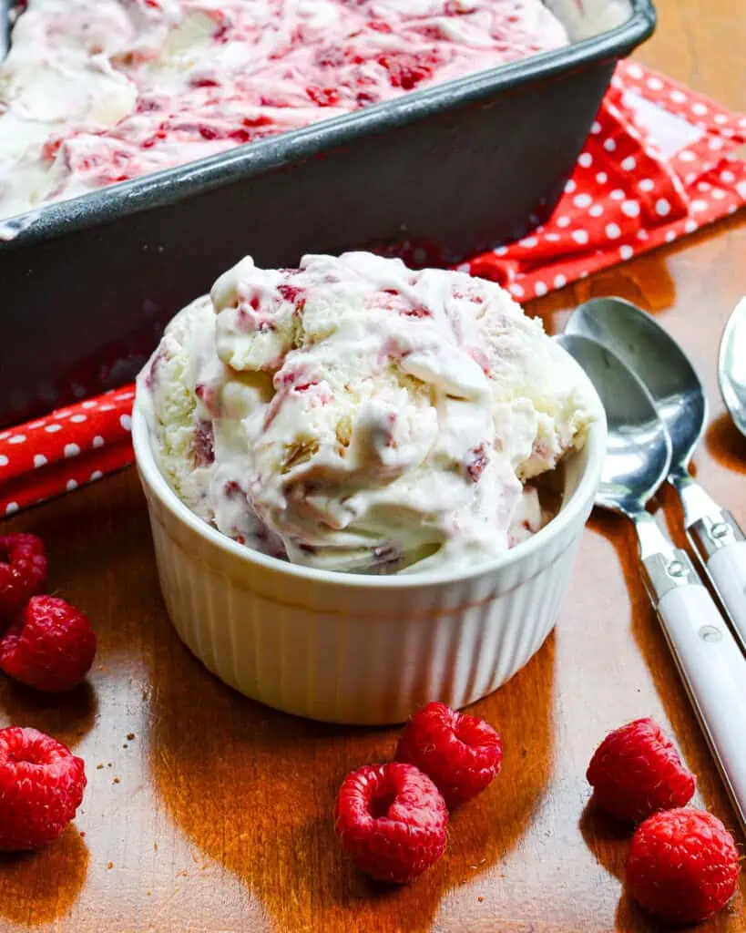 An overhead view of a bowl full of raspberry ice cream with a loaf pan full of raspberry ice cream in the background. 