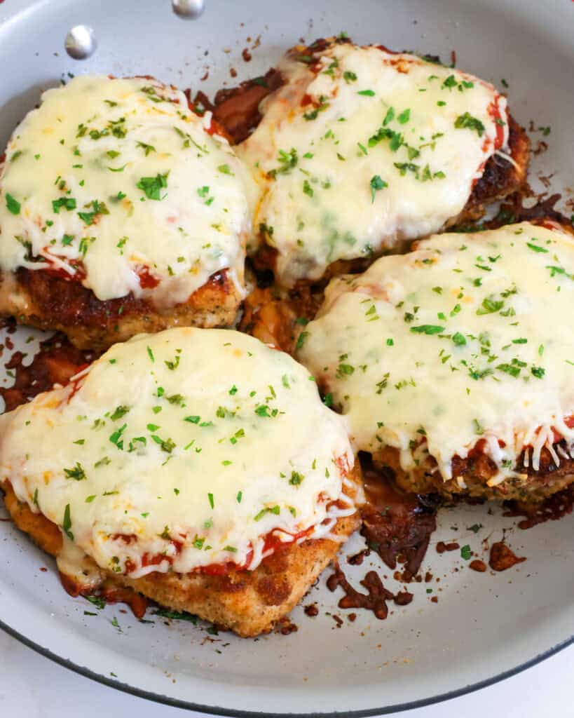A large skillet full of breaded browned chicken breasts with marinara, mozzarella, and provolone.
