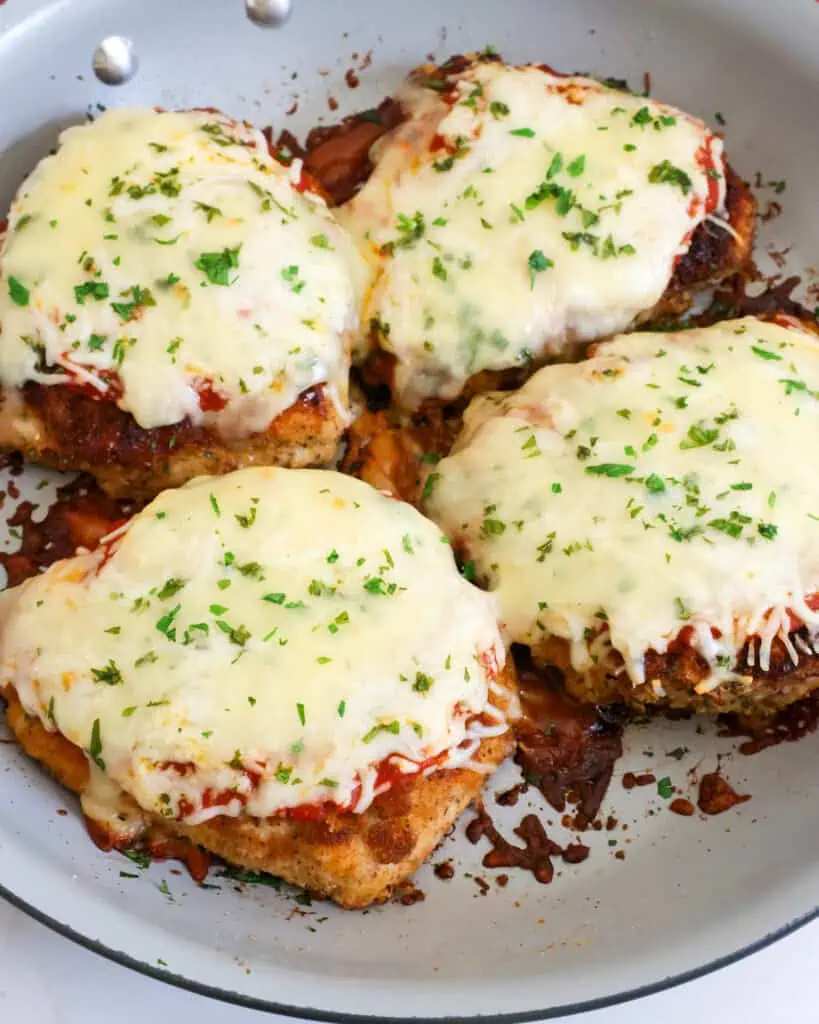 A large skillet full of breaded browned chicken breasts with marinara, mozzarella, and provolone. 