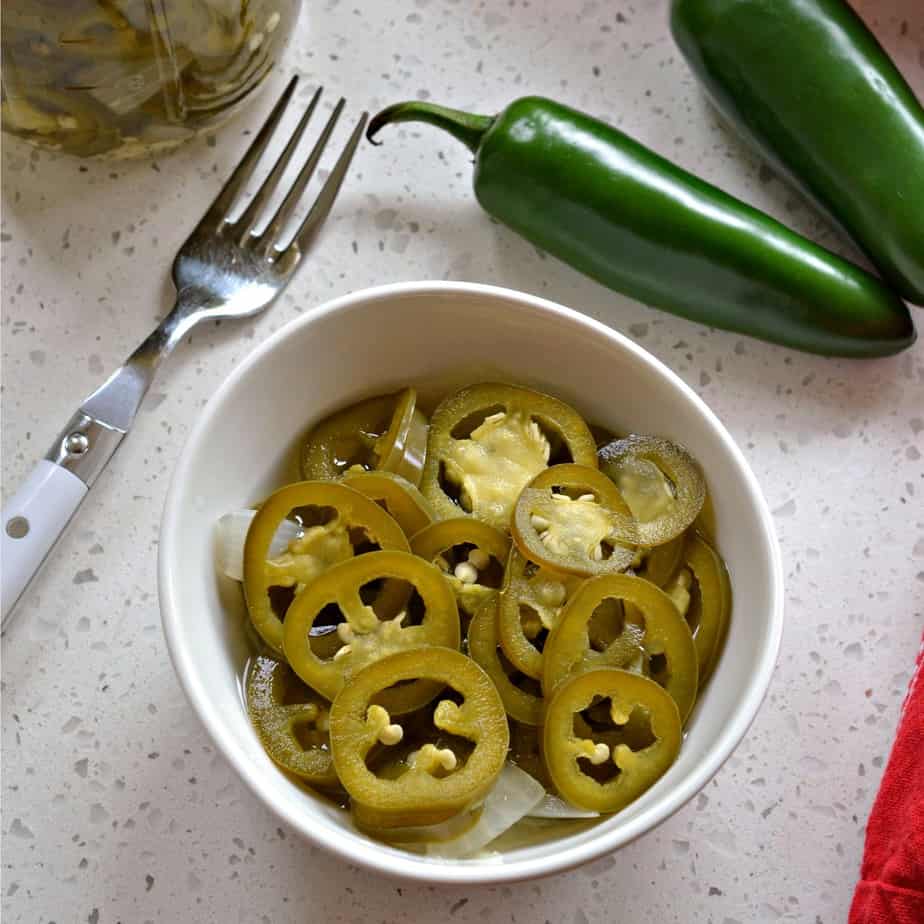 Jalapenos that have been pickled in a bowl along with fresh ones on the counter