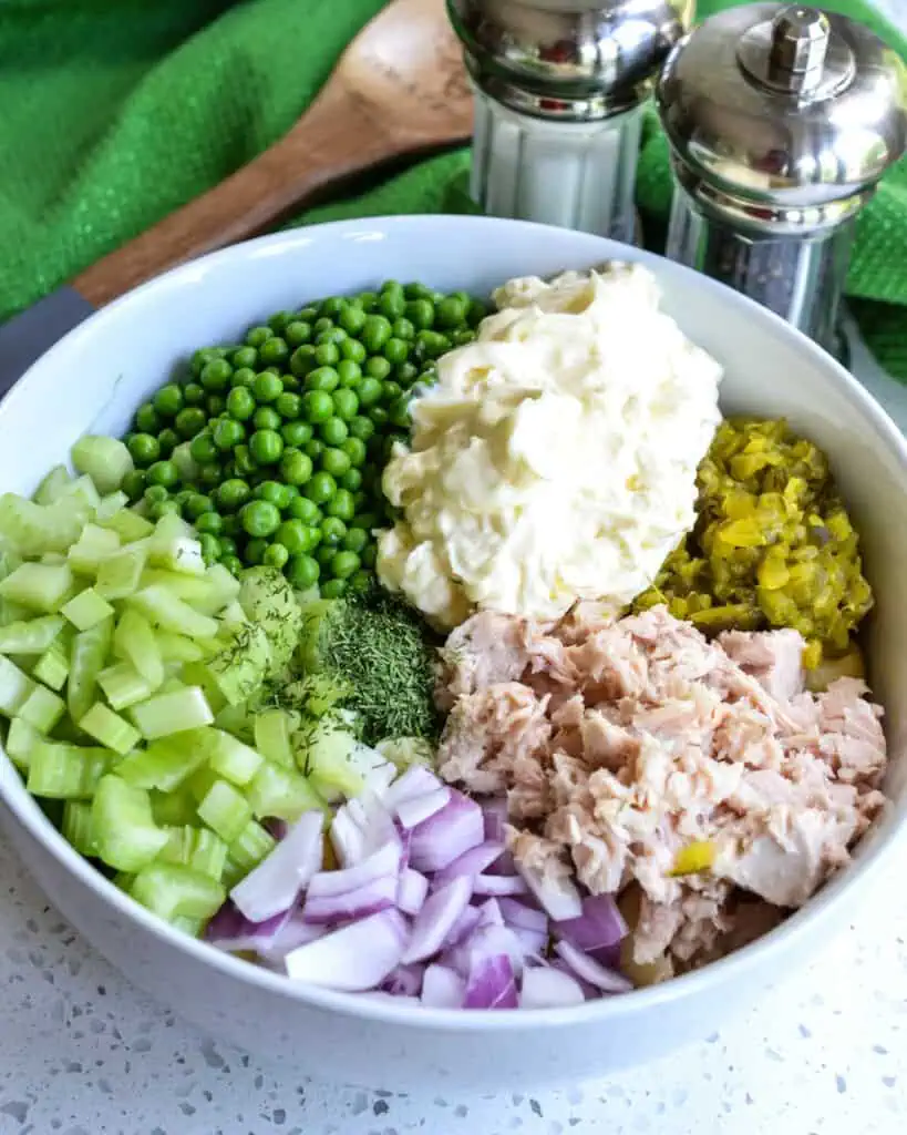 All the ingredients in a large serving bowl with a salt and pepper shaker, green towel, and wooden spoon, in the background