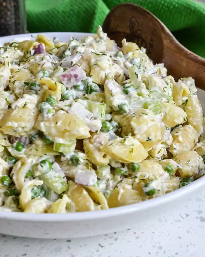 A close up veiw of tuna pasta salad with peas, pickle relish, celery, red onion, dill, and mayonnaise. 