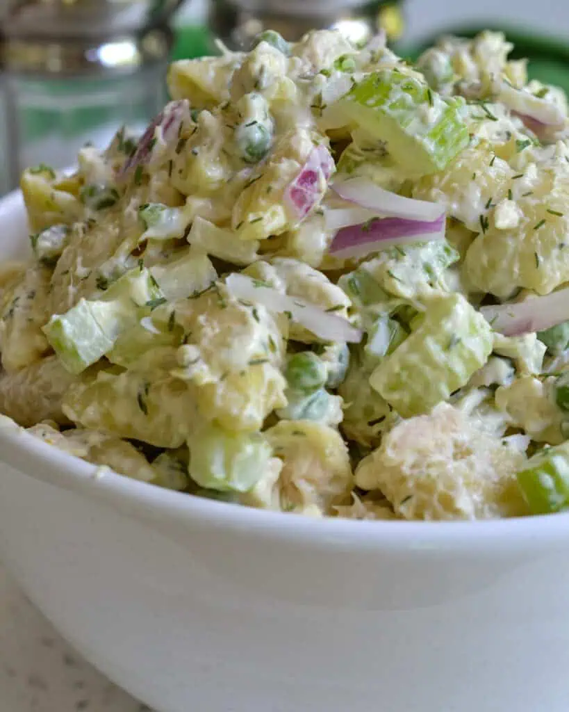 A close up view of a white serving bowl full of tuna salad. . 