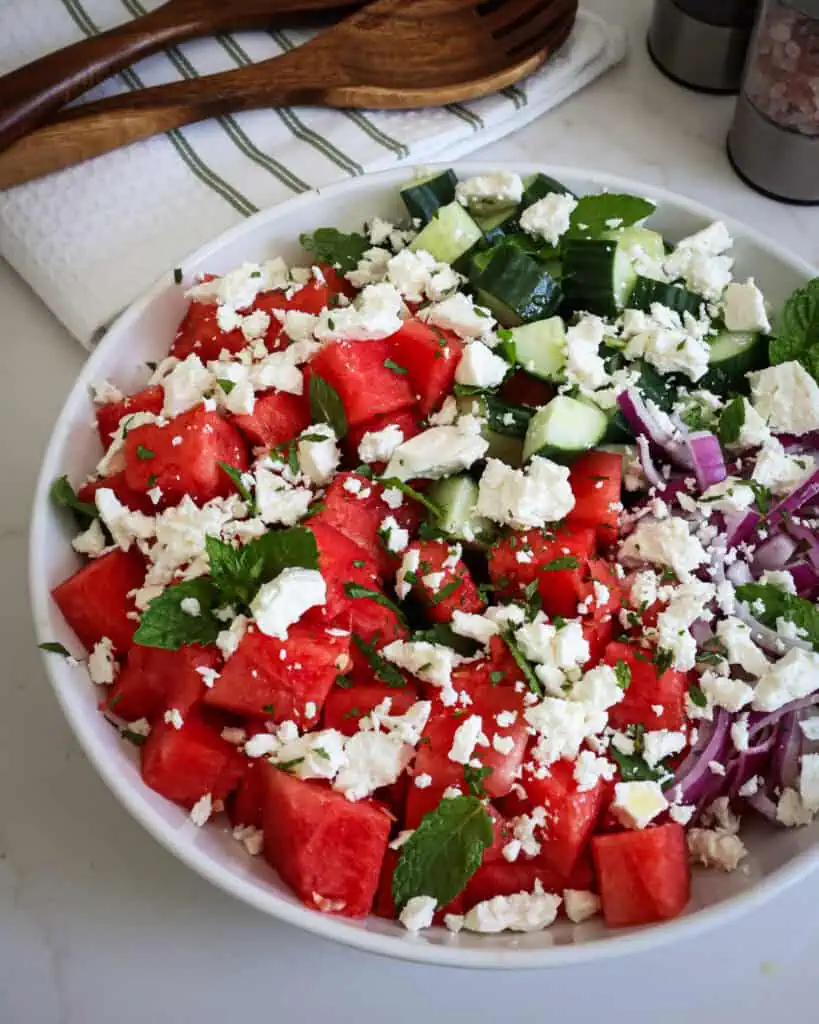 A close up view of watermelon salad with crisp cucumber, salty feta cheese, sweet red onion, garden-fresh mint, and sweet watermelon in a lightly sweetened lime drizzle.