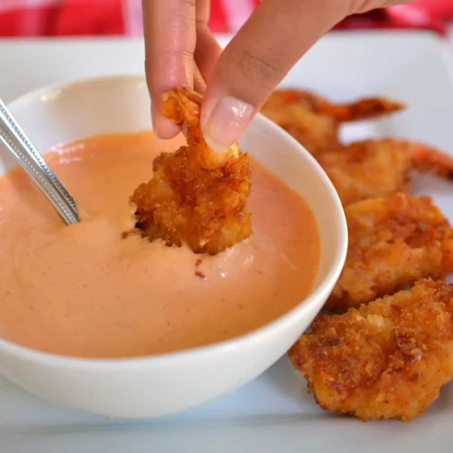 A deep fried shrimp being dipping into a bowl of sriracha mayonnaise.