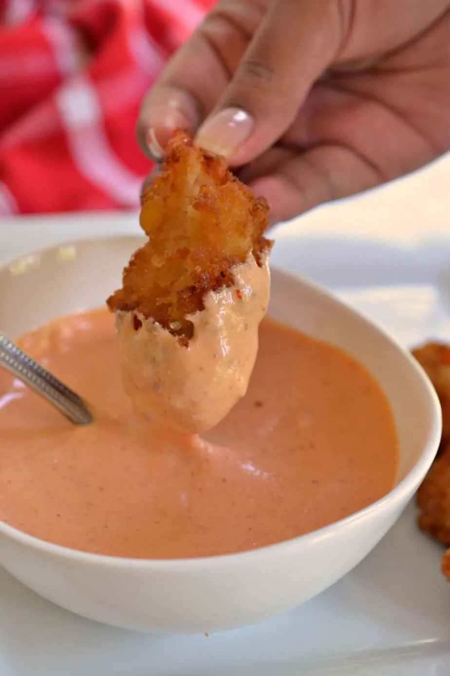 A bowl of sriracha mayonnaise wiht a golden fried shrimp dipped in it. 