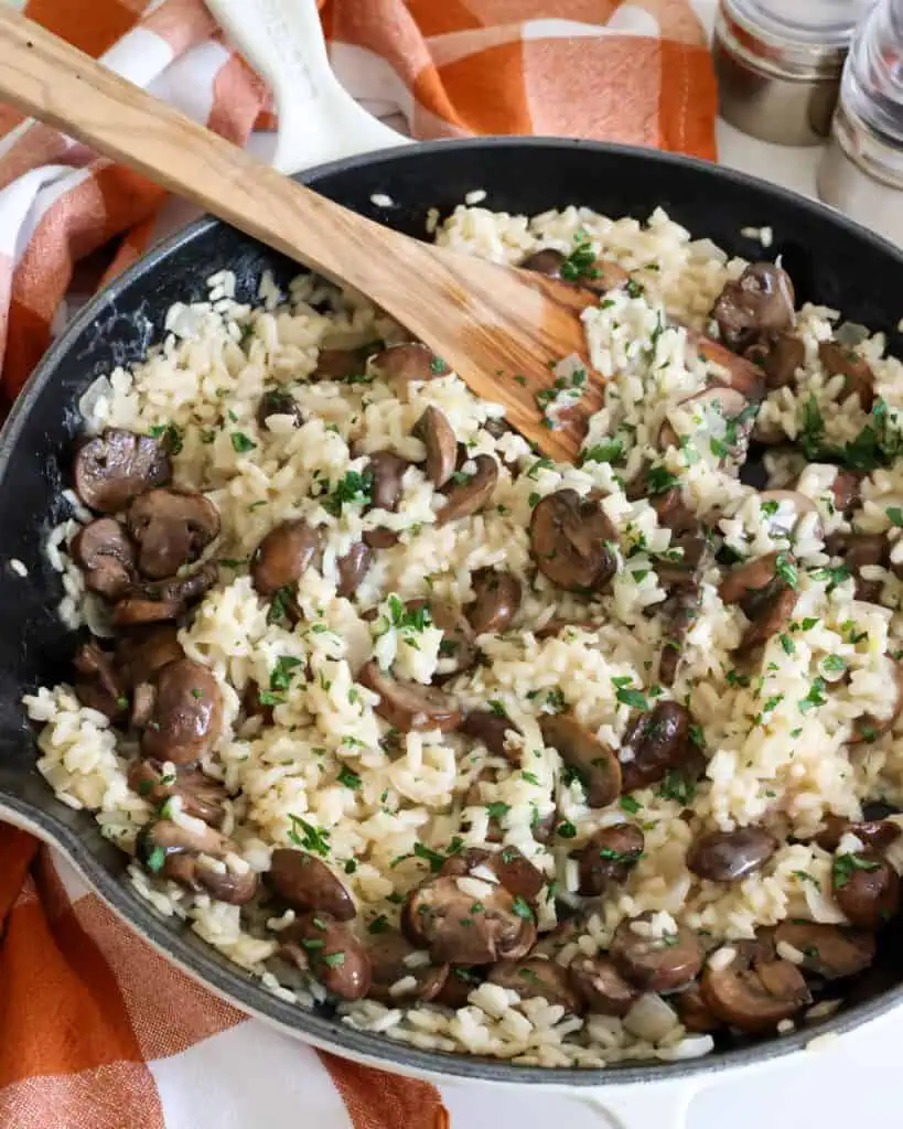 A large skillet full of mushroom risotto with a salt and pepper mill in the background.