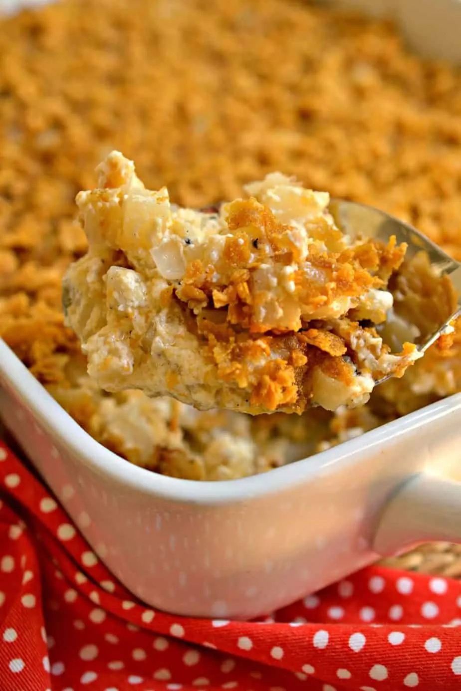 A casserole dish and a large serving spoon full of funeral potatoes. 