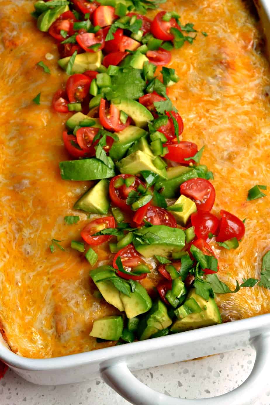 The top of the enchilada casserole garnish with chopped avocado, tomato, and cilantro. 