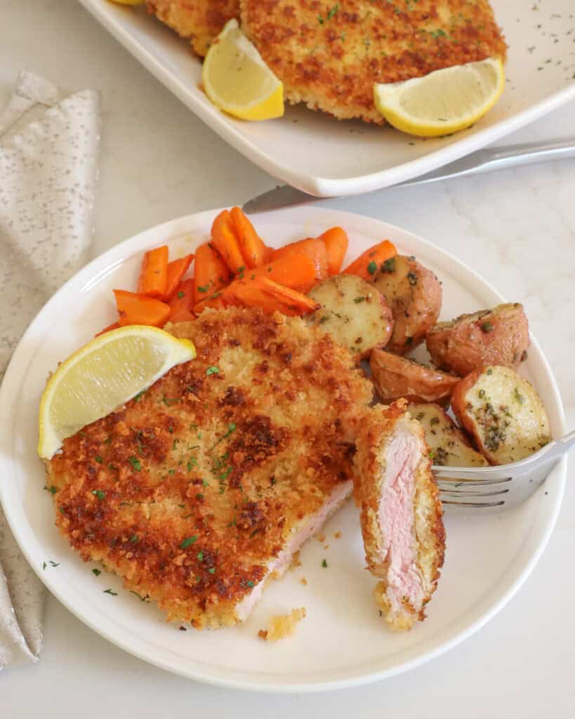 An overhead view of pork schnitzel on a plate with a slice cut off of it.  