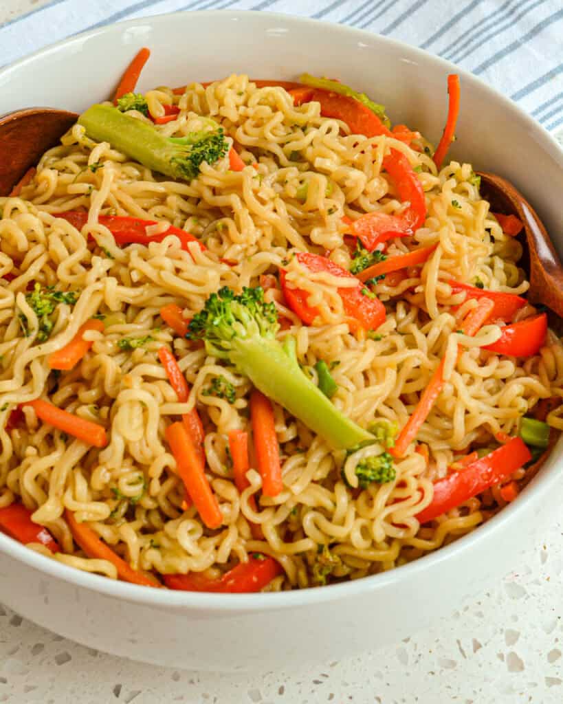 A bowl full of ramen noodle stir-fry  with bell peppers, carrots and broccoli.