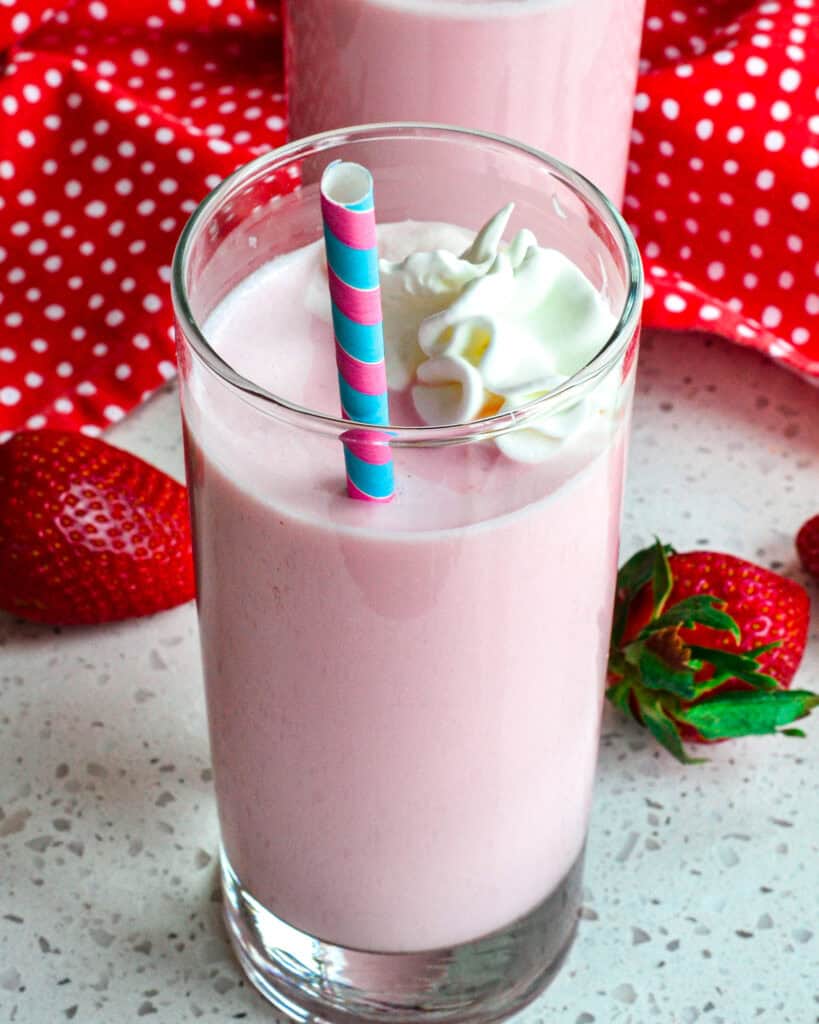 Close up view of strawberry milk topped with whipped cream. 
